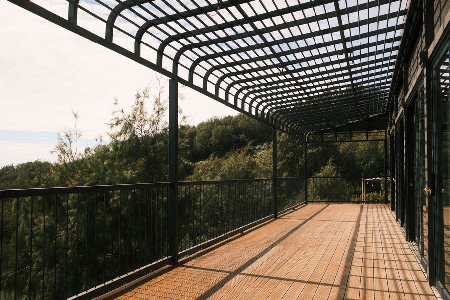 Covered wooden walkway with black railing and arched trellis overlooking a green hillside