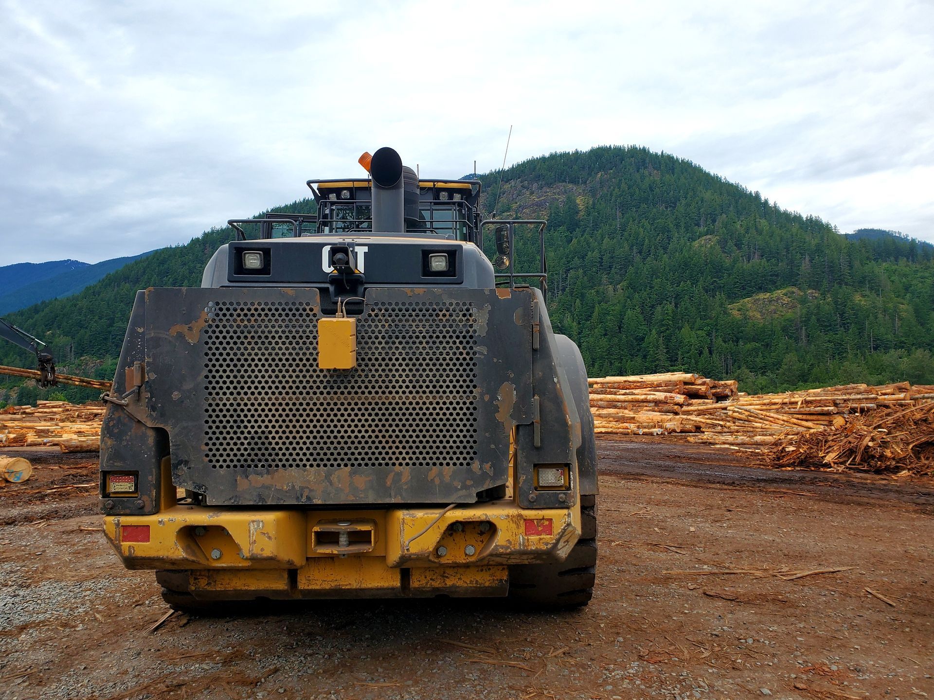 Large yellow forestry equipment on dirt road with forested hills in the background