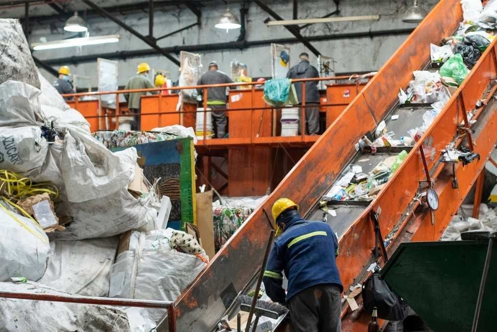 Workers sorting waste on an industrial recycling conveyor with orange machinery and trash bags