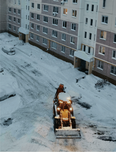 Wheel loader doing construction near an apartment in a snowy environment