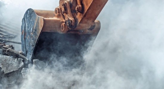 Excavator bucket digging through a cloud of dust and debris on a construction site