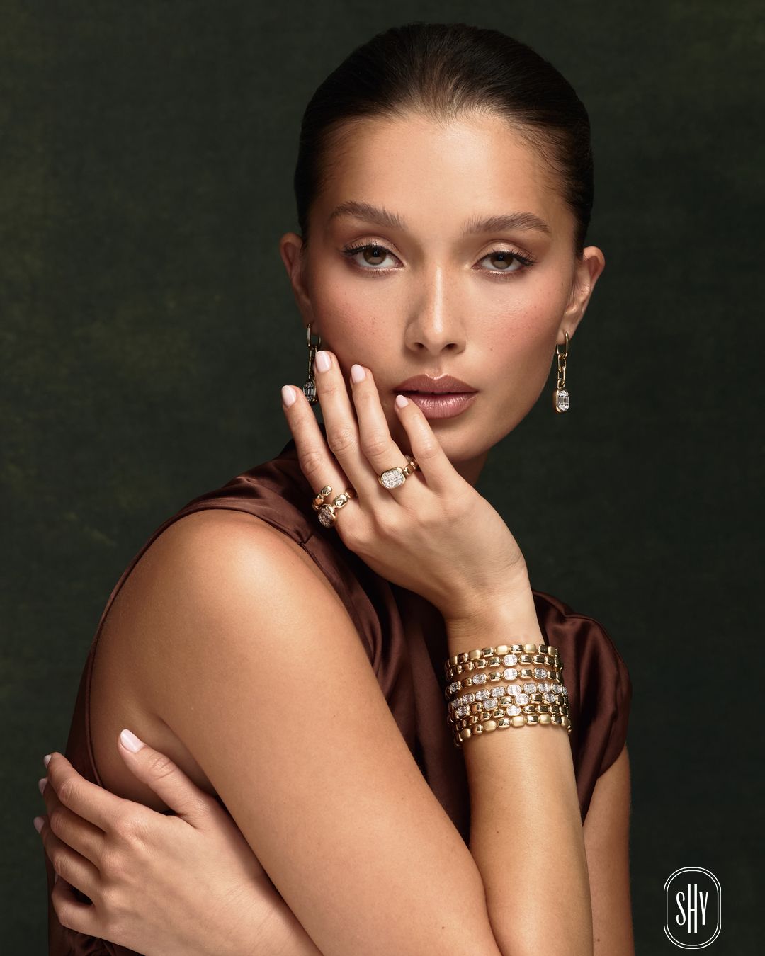 Portrait of a woman in a dark dress, wearing gold jewelry, posed against a dark background.