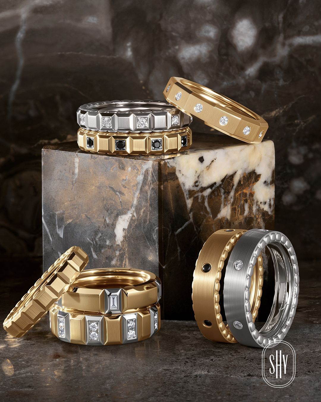 Gold and silver diamond-studded rings and bands arranged on a dark marble pedestal.