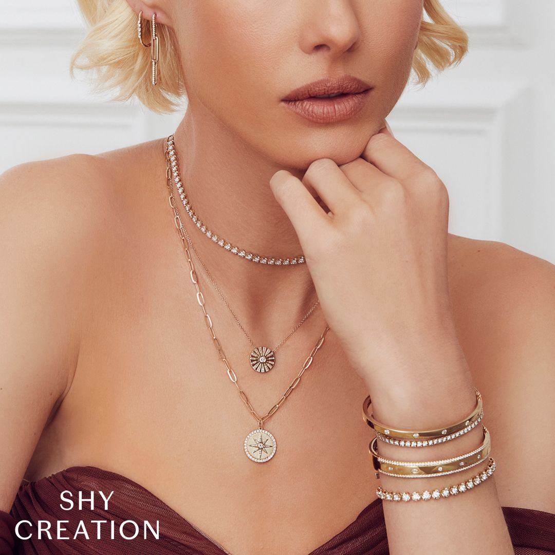 Close-up of a curly-haired model wearing silver jewelry, posing against a soft beige background.
