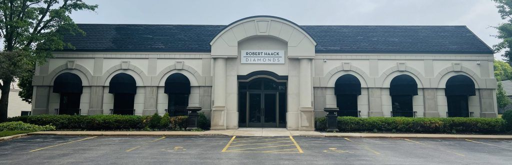 Front view of a white building with arched windows, dark roof, and a parking lot in front.