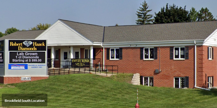 Front view of a white building with arched windows, dark roof, and a parking lot in front.