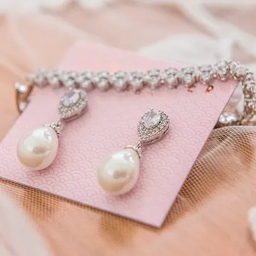 Pink jewelry case with pearl drop earrings and a sparkling necklace on a soft fabric background
