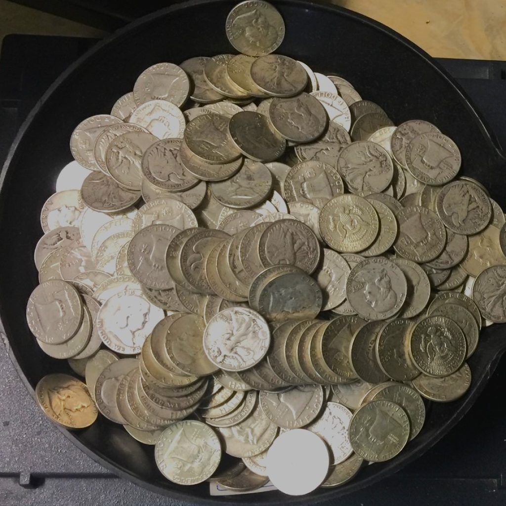 A shallow tray piled high with assorted coins and tokens in silver, gold, and white.
