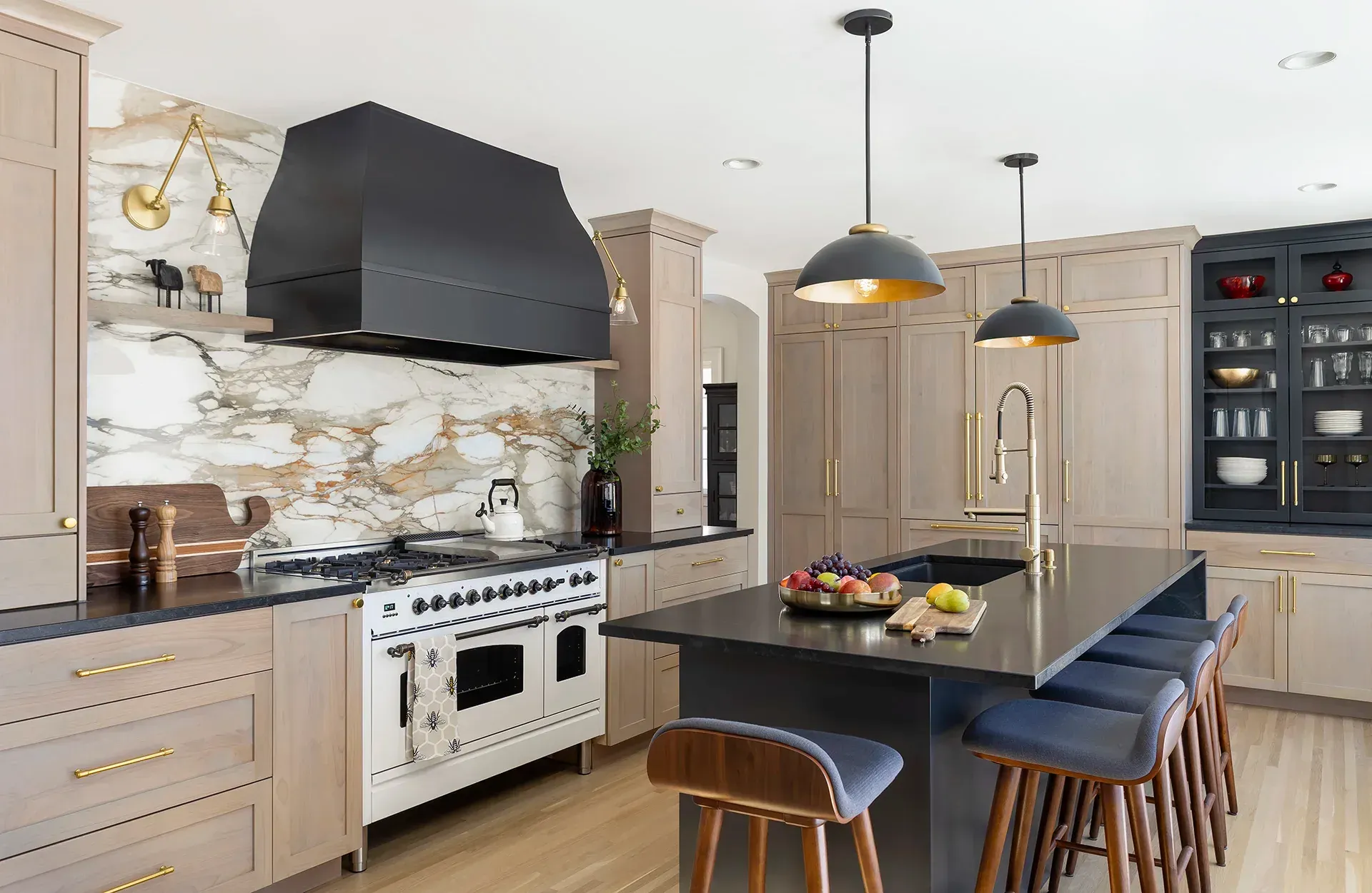 Modern kitchen with black range hood, marble backsplash, island, and dark stools