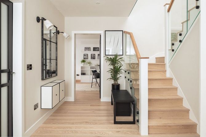 Bright hallway with staircase, mirror, bench, and light wood floors in a modern home.