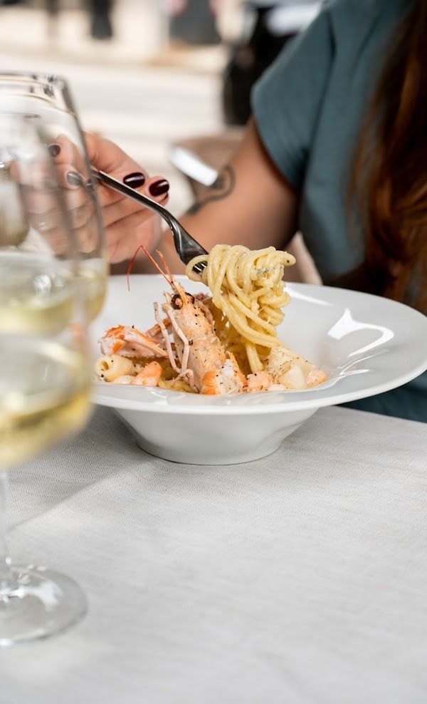 Una mano serve la pasta su un piatto bianco a un tavolo di ristorante.