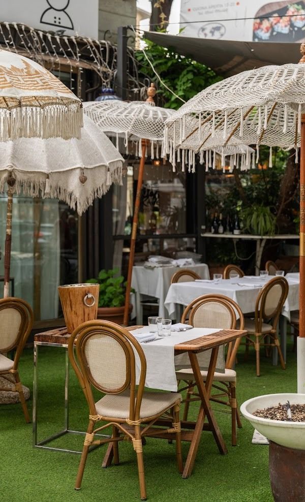 Tavolini da caffè all'aperto con sedie in vimini, ombrelloni di pizzo bianco e tovaglie bianche su prato verde.