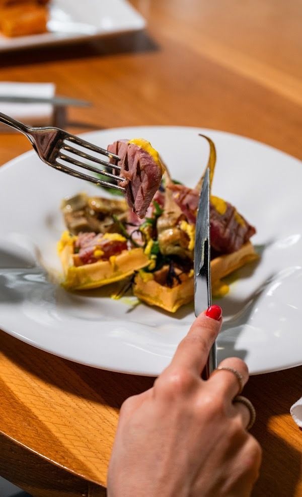 Taglio a mano di un piatto di carne con salsa gialla su un tavolo di legno
