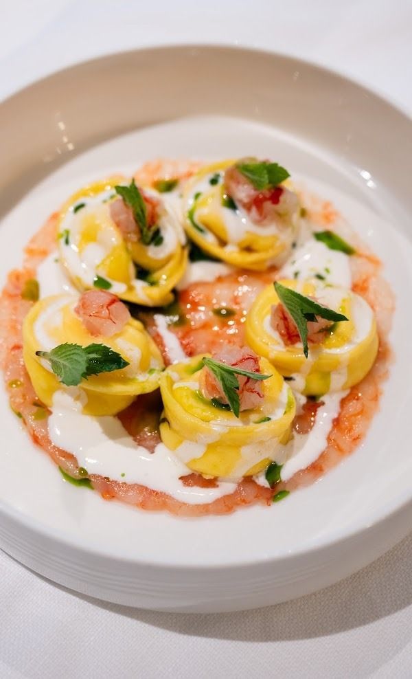 Ravioli con salsa cremosa, pomodori ed erbe aromatiche serviti su un piatto bianco.