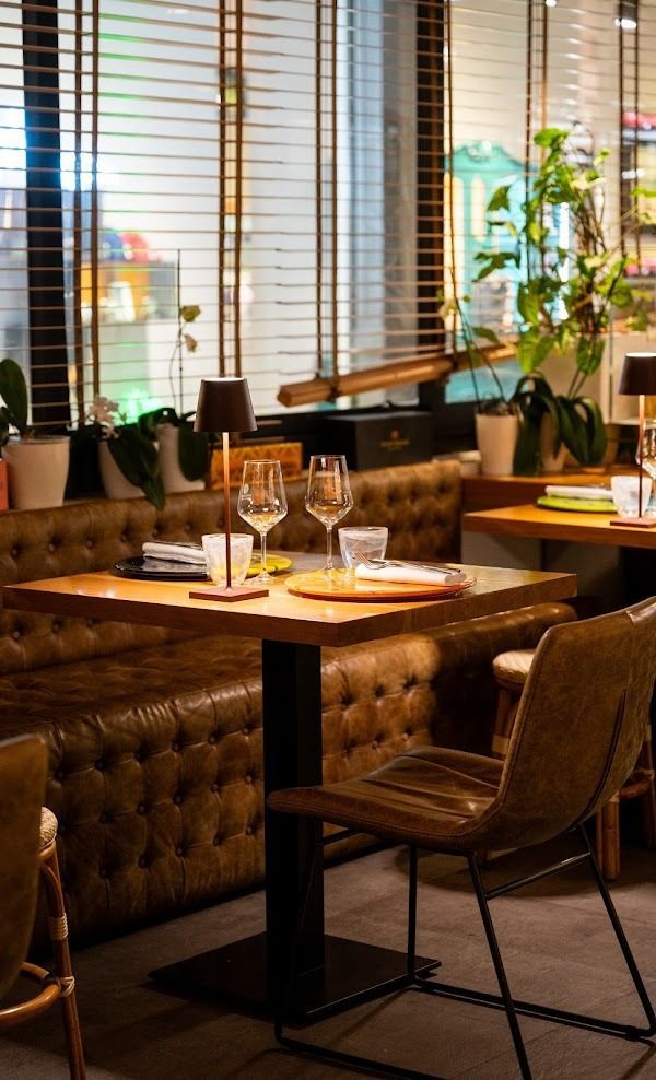 Accogliente angolo ristorante con tavolo apparecchiato, bicchieri da vino, sedie in pelle e tende alle finestre.