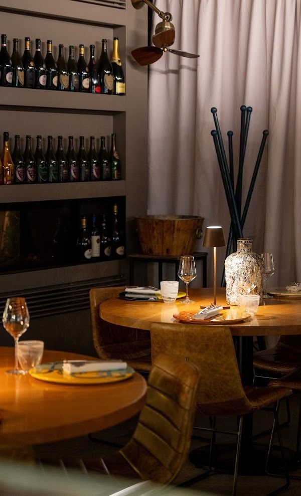 Un accogliente tavolo da ristorante apparecchiato con candele, bicchieri da vino e scaffali di bottiglie sullo sfondo.