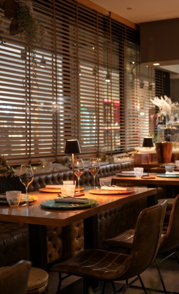 Accogliente sala da pranzo del ristorante con tavoli apparecchiati, calici da vino e tende alle finestre al crepuscolo.