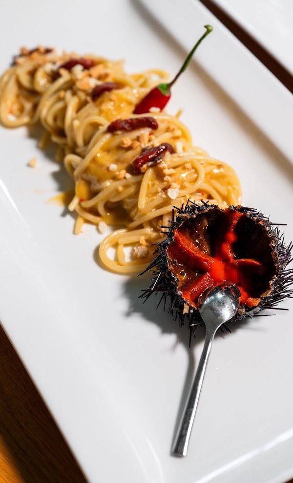 Spaghetti su un piatto bianco con salsa rossa e guarnizione di un guscio di riccio di mare nero e spinoso, serviti con un cucchiaio.