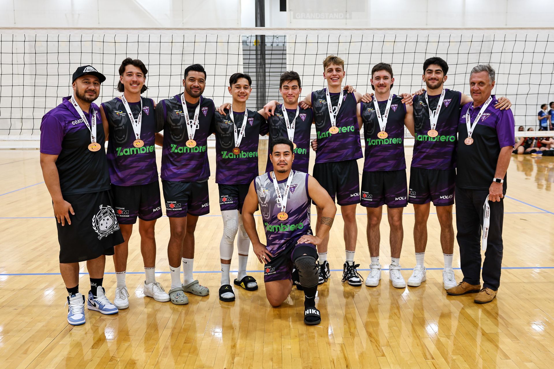 A group of men are posing for a picture on a volleyball court.