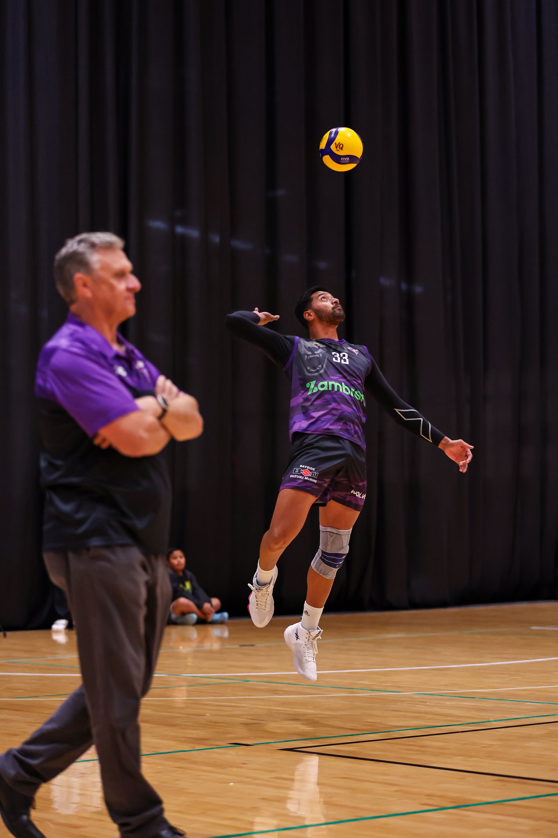 A man is standing next to a volleyball player on a court.