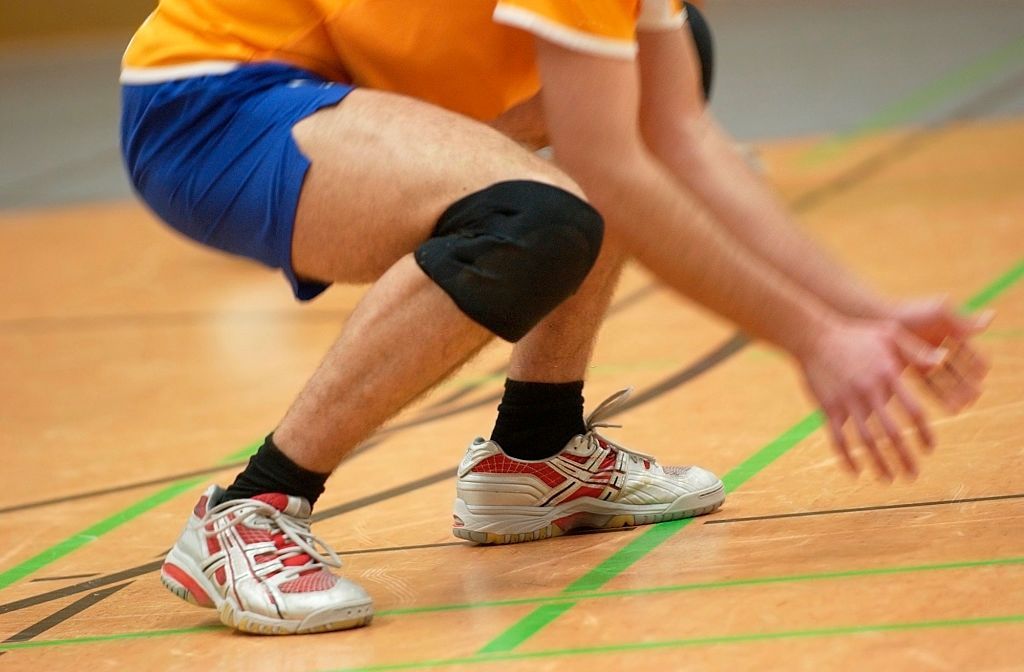 A man wearing knee pads is squatting on a basketball court.