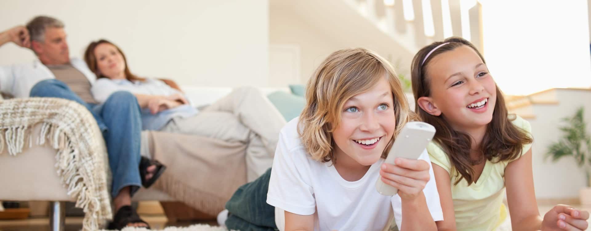 A boy and two girls are laying on the floor watching tv.