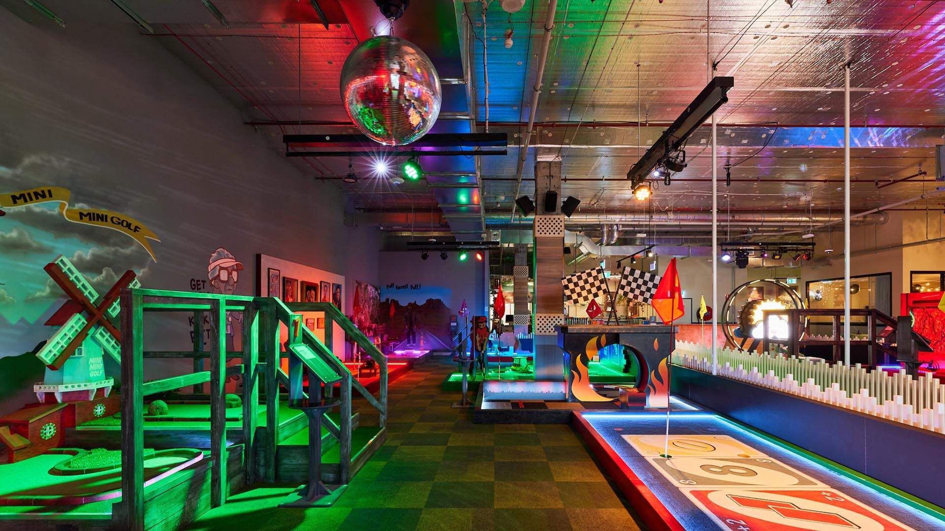 A mini golf course in a dark room with a disco ball hanging from the ceiling.