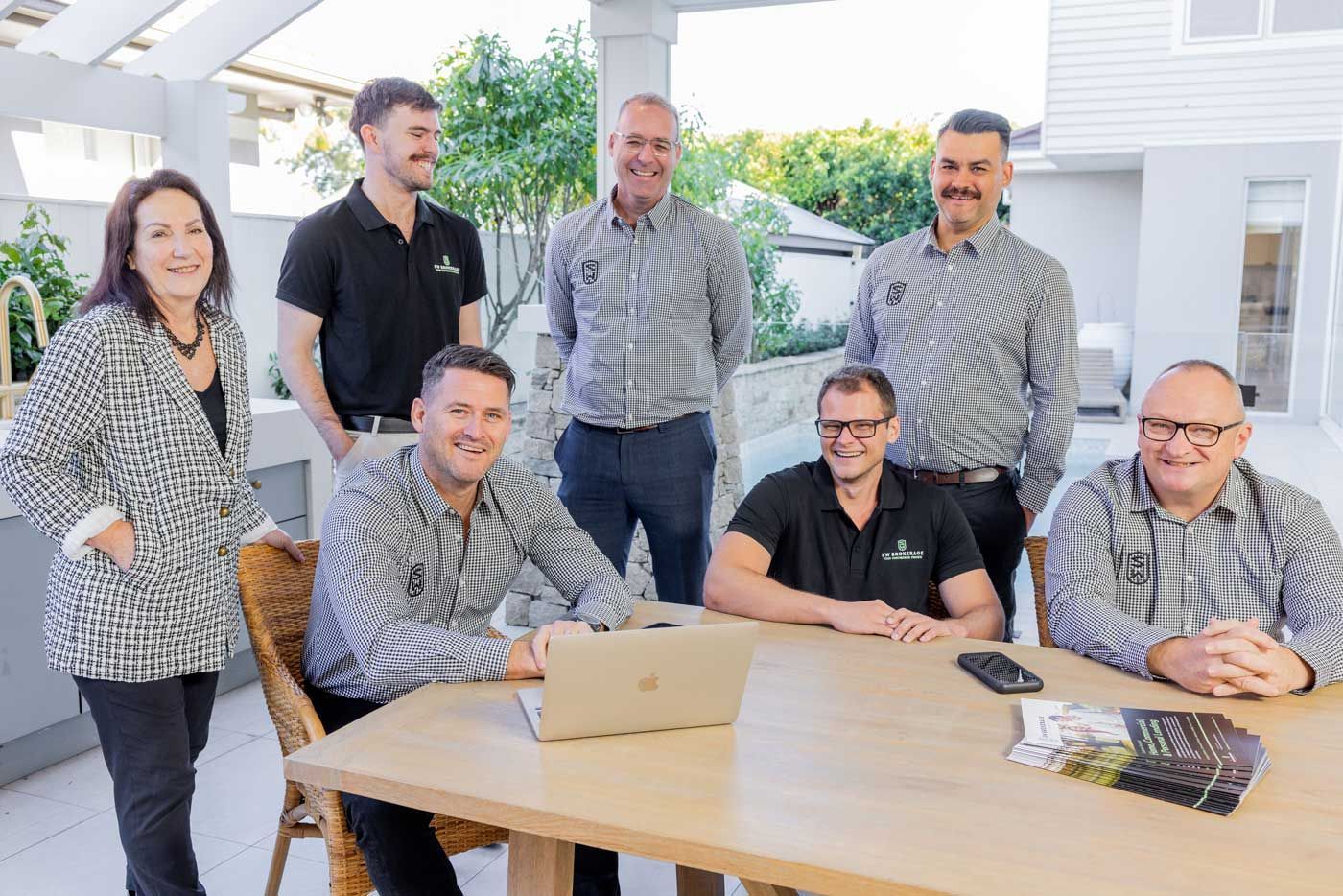 A group of people are sitting around a table with a laptop.