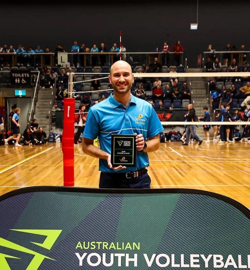 A man is holding a trophy in front of an australian youth volleyball banner