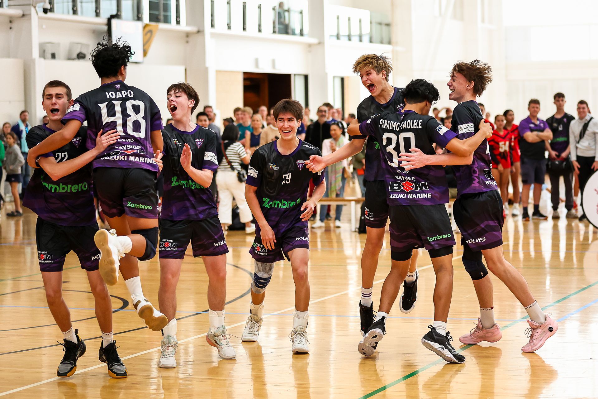 A group of young men are hugging each other on a basketball court.