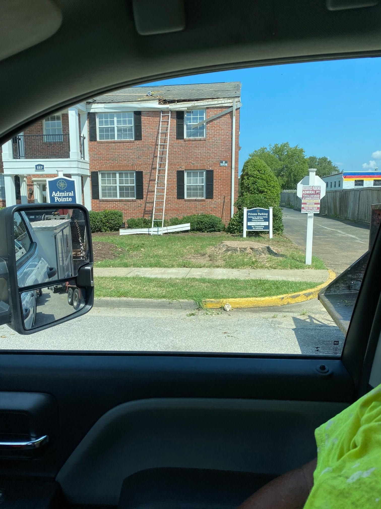 View from a car window of a brick apartment building and sign near a driveway on a sunny day