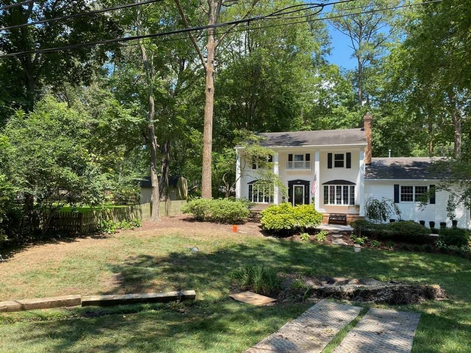 White two-story house with columns and porch, surrounded by trees and a grassy yard.