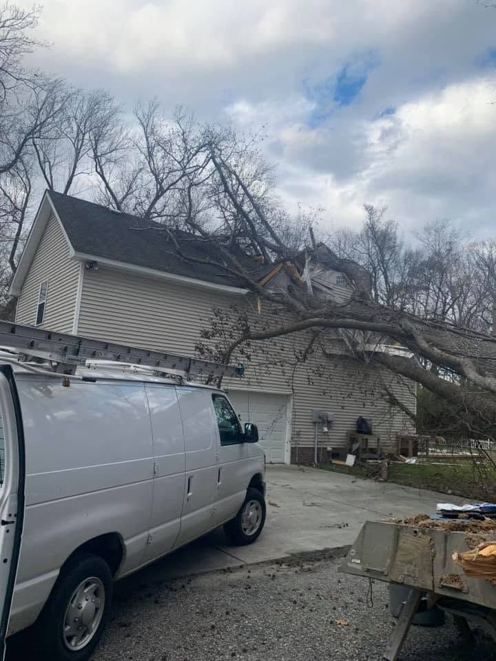 White van parked beside a house hit by a fallen tree after storm damage