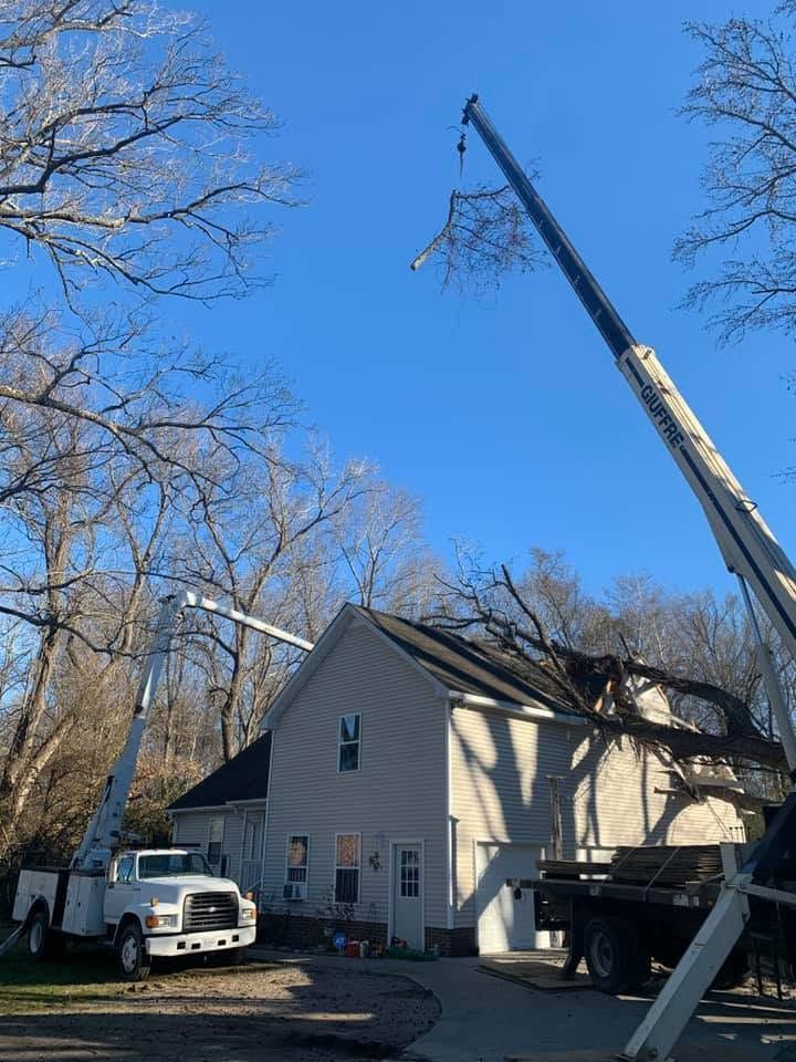Crane lifting roof materials beside a beige house under a clear blue sky, with a truck parked nearby.