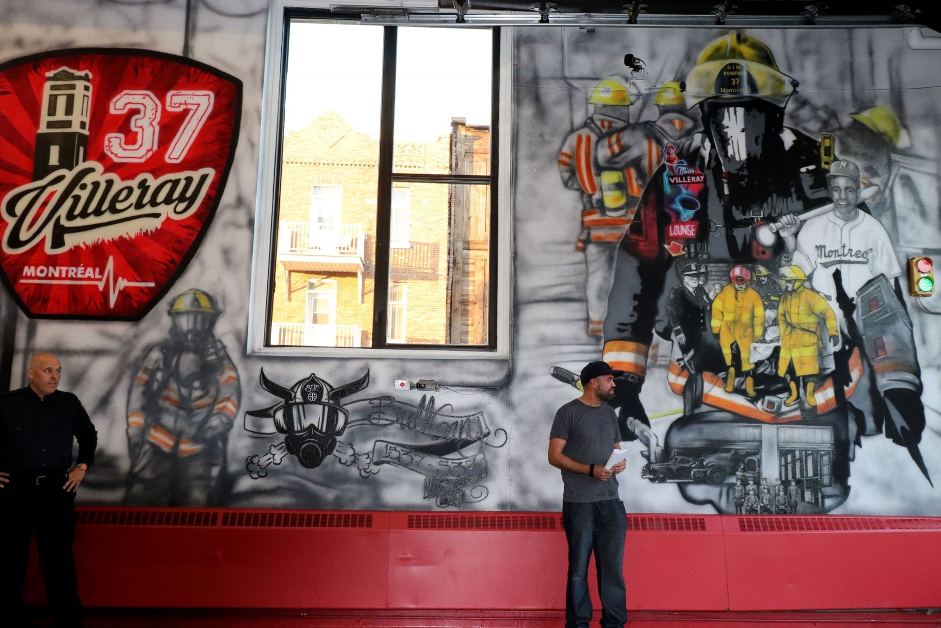 A man is standing in front of a wall with a mural of firefighters on it.