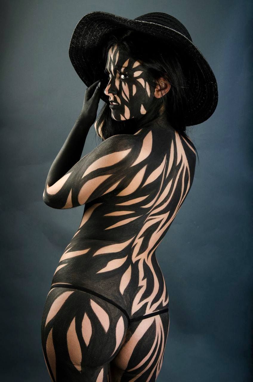 A woman with her body painted black and white is wearing a hat.