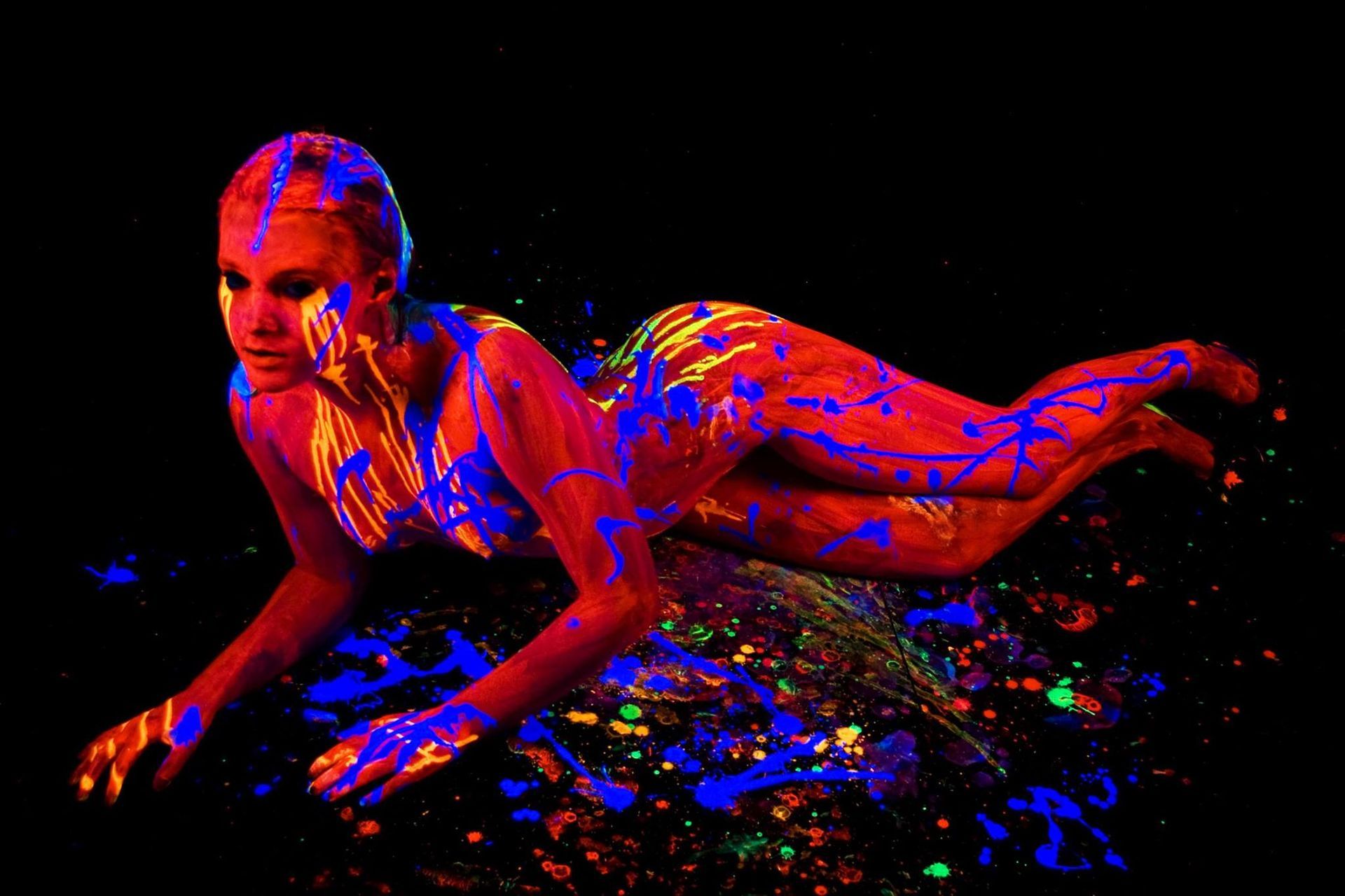 A woman is laying on the floor with glow in the dark paint on her body.