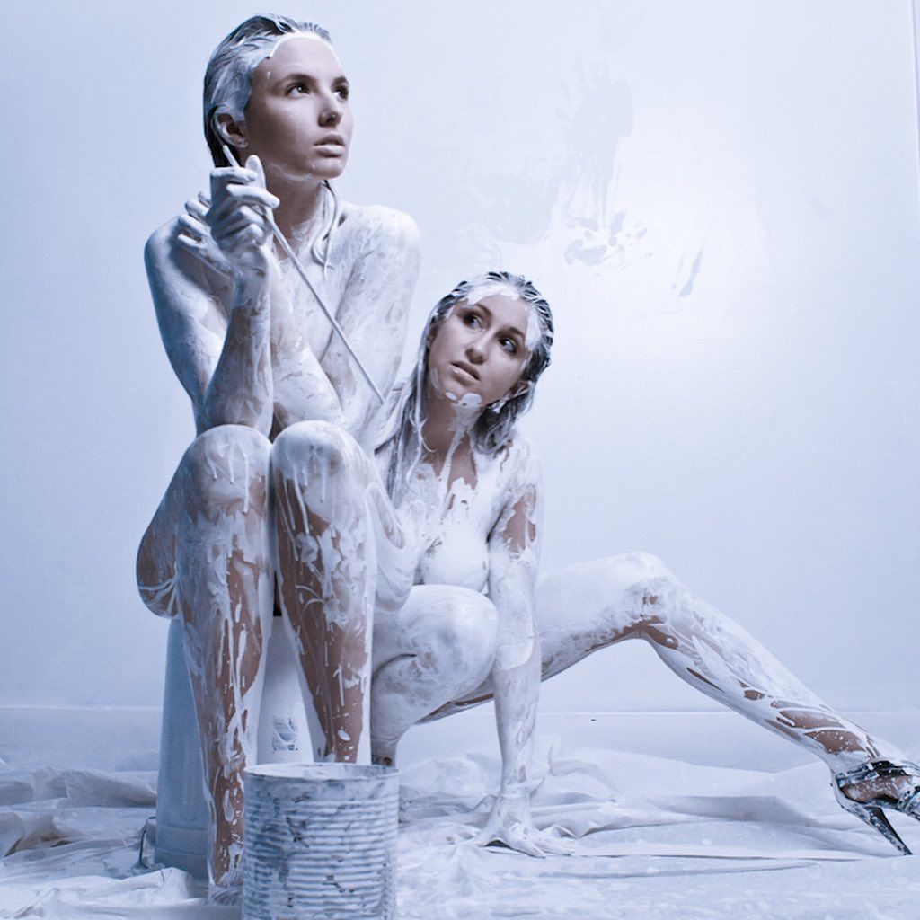 Two women covered in white paint are sitting next to each other