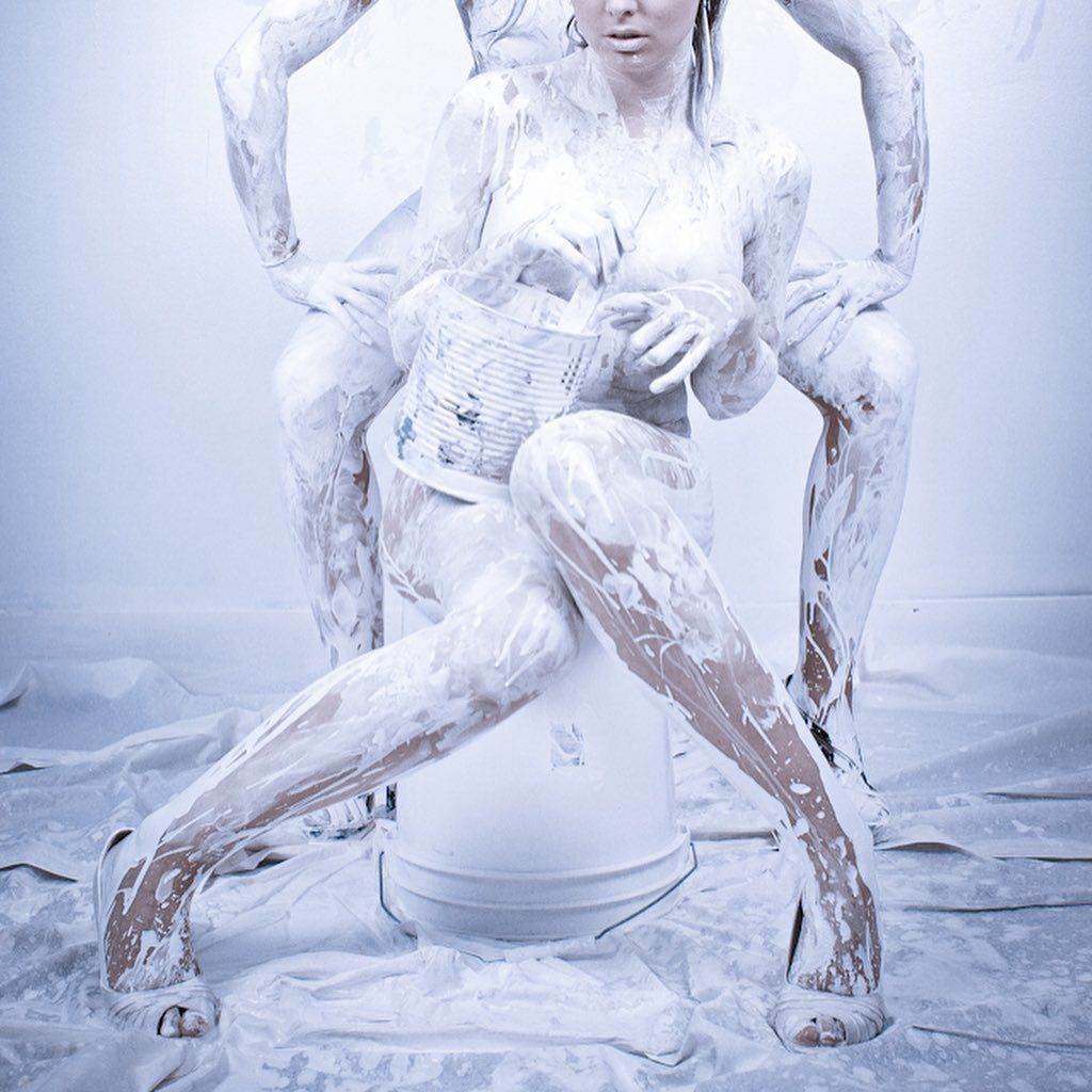 A woman covered in white paint is sitting on a bucket