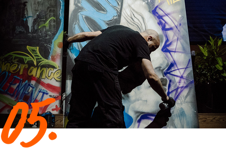 Un homme peint des graffitis sur un mur avec le numéro 05 en dessous de lui