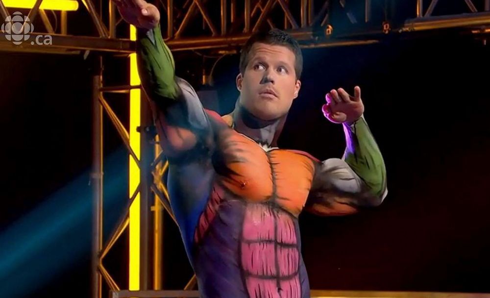 A man in a body painted superhero costume is standing on a stage.