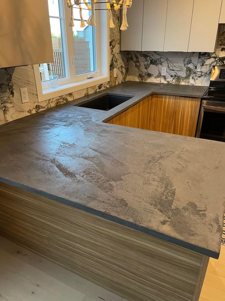 A kitchen with a concrete counter top and a sink.
