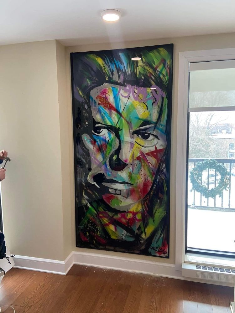 A large painting of a man 's face is hanging on a wall next to a window.