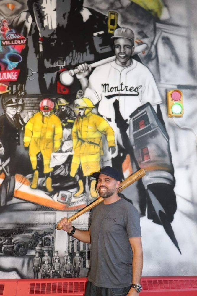 A man holding a bat in front of a montreal mural