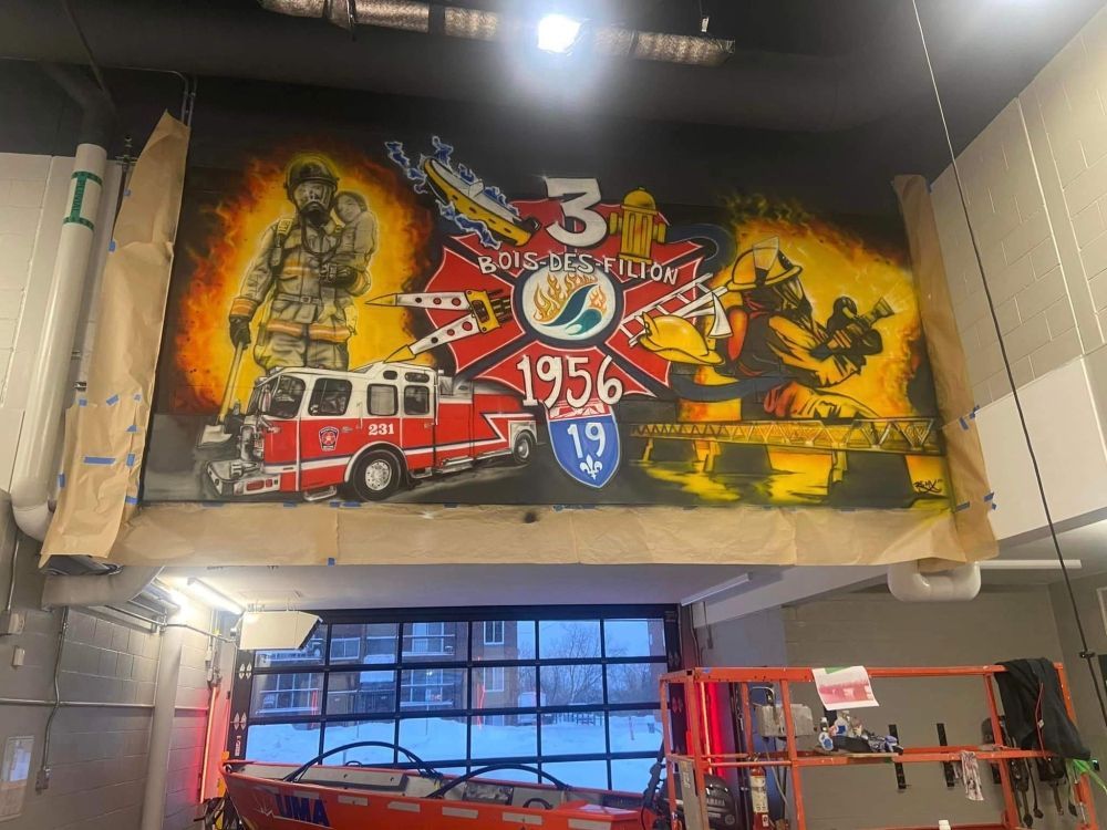 A mural of firefighters is being painted on the wall of a fire station.