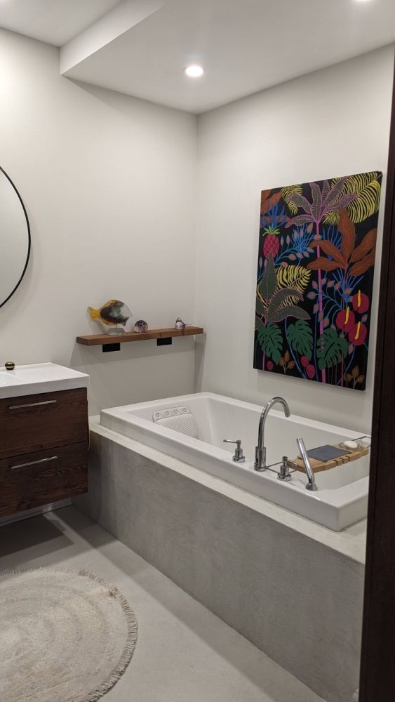 A bathroom with a bathtub , sink , mirror and painting on the wall.