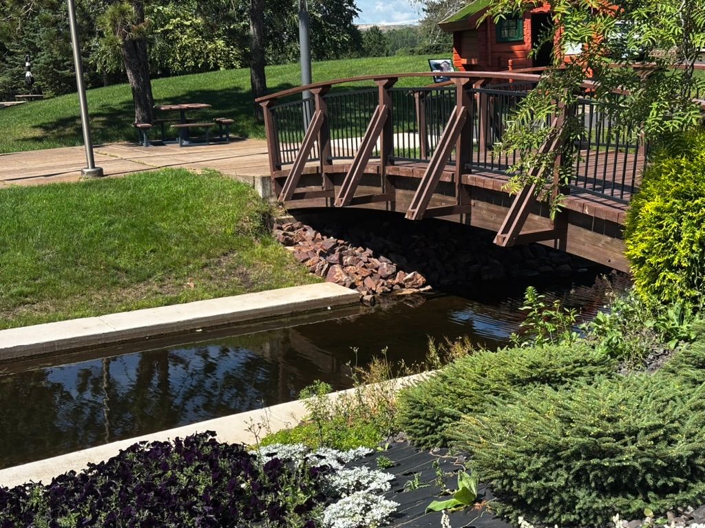 Wooden footbridge over a small stream in a landscaped garden with green grass and shrubs