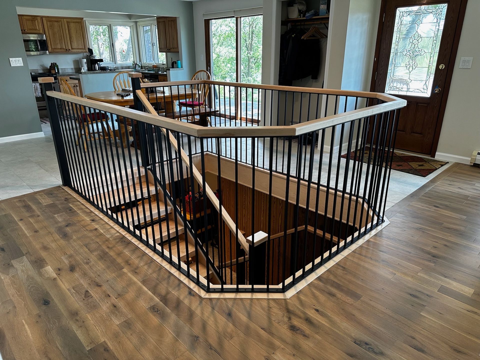 Open stairwell with black railing in a bright home interior and hardwood floors