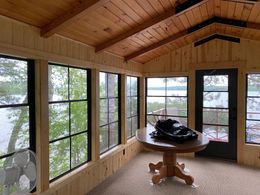 A bright room with large windows overlooking a snowy, tree-filled landscape, featuring indoor plants and part of a bed.