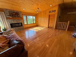 Wood-paneled living room with stone fireplace, large window, leather sofa, and sunlight on hardwood floors
